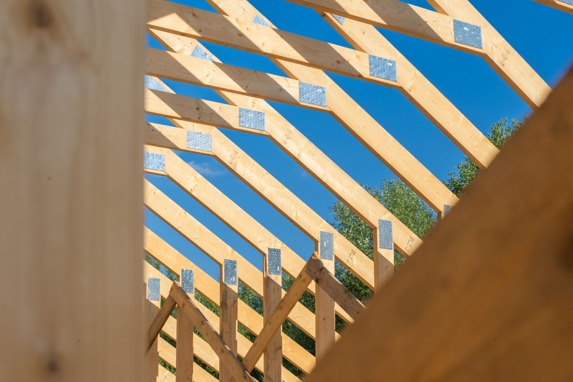 Workers construct a wooden roof framework at a building site, showcasing modern techniques. The clear blue sky adds to the bright and productive atmosphere.